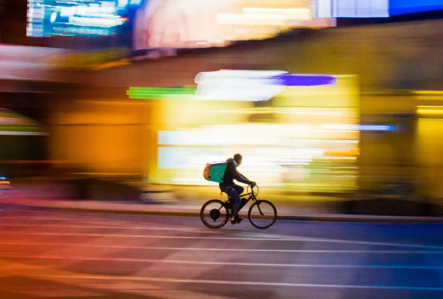 Cyclist courier in motion at night, with blurred lights and buildings from a long exposure.
